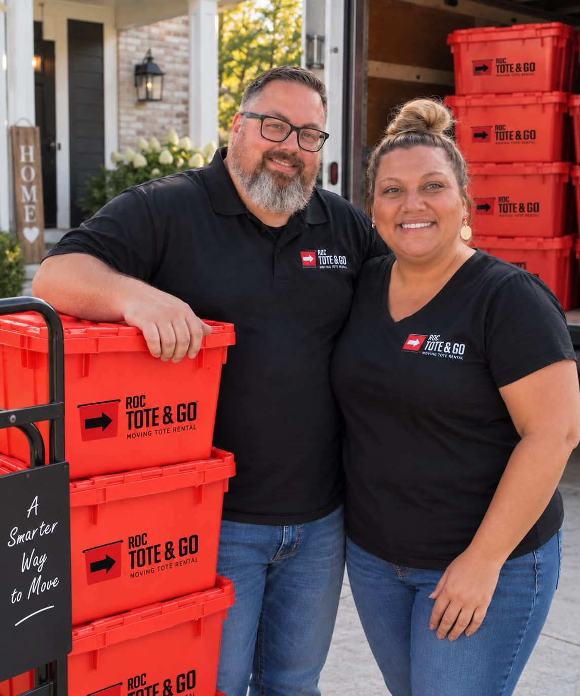 Steph and Sean, the owners of ROC Tote &amp; Go, standing beside stacks of red moving totes on delivery day
