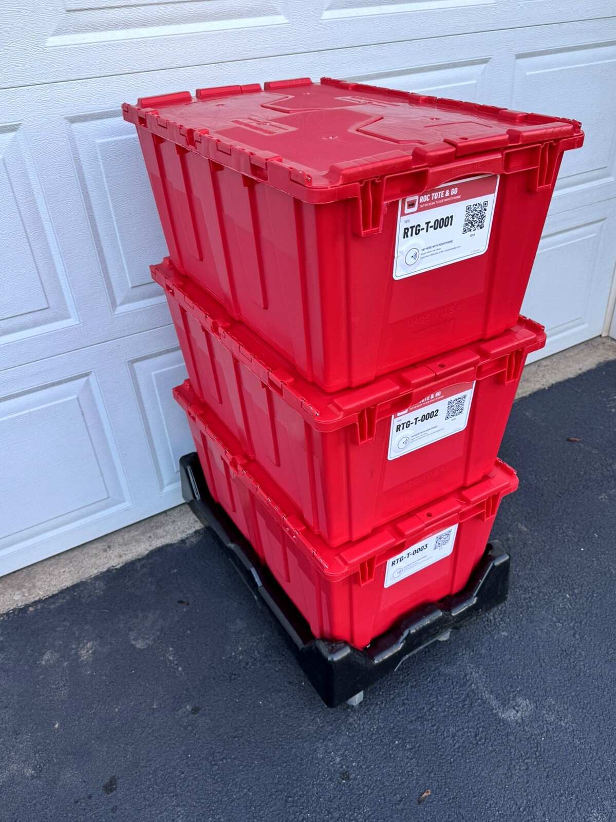 Three red moving totes with attached red lids stacked on a black dolly, labels facing out
